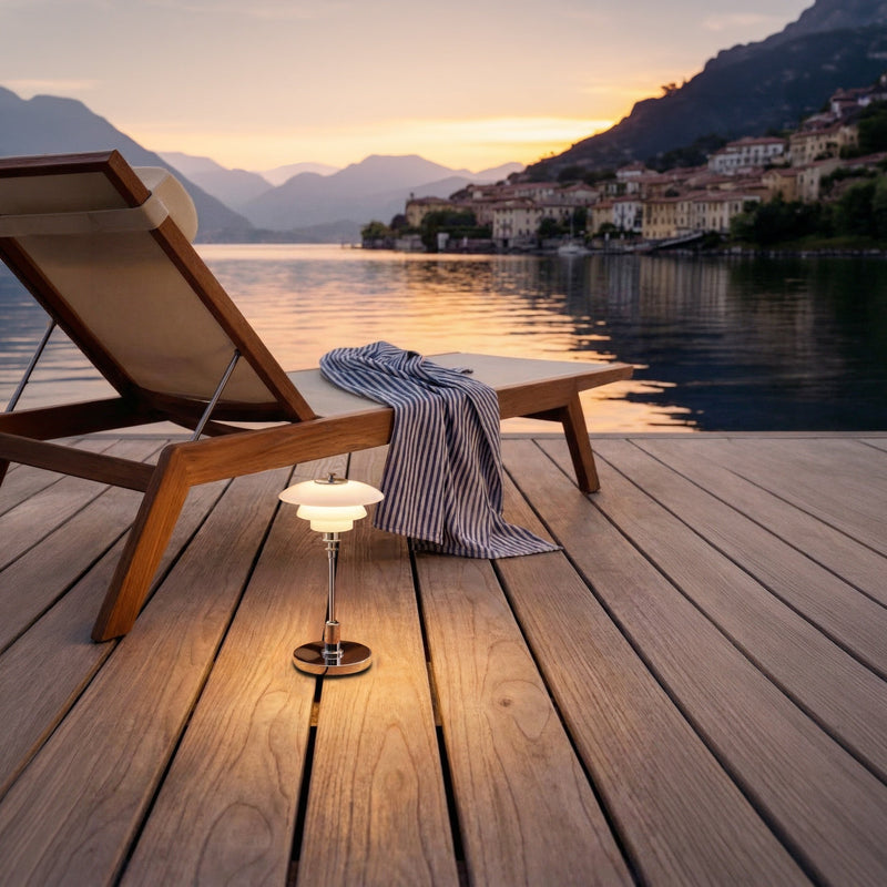 Chrome PH 1/1 Portable Lamp beside a lounge chair overlooking the lake at dusk.