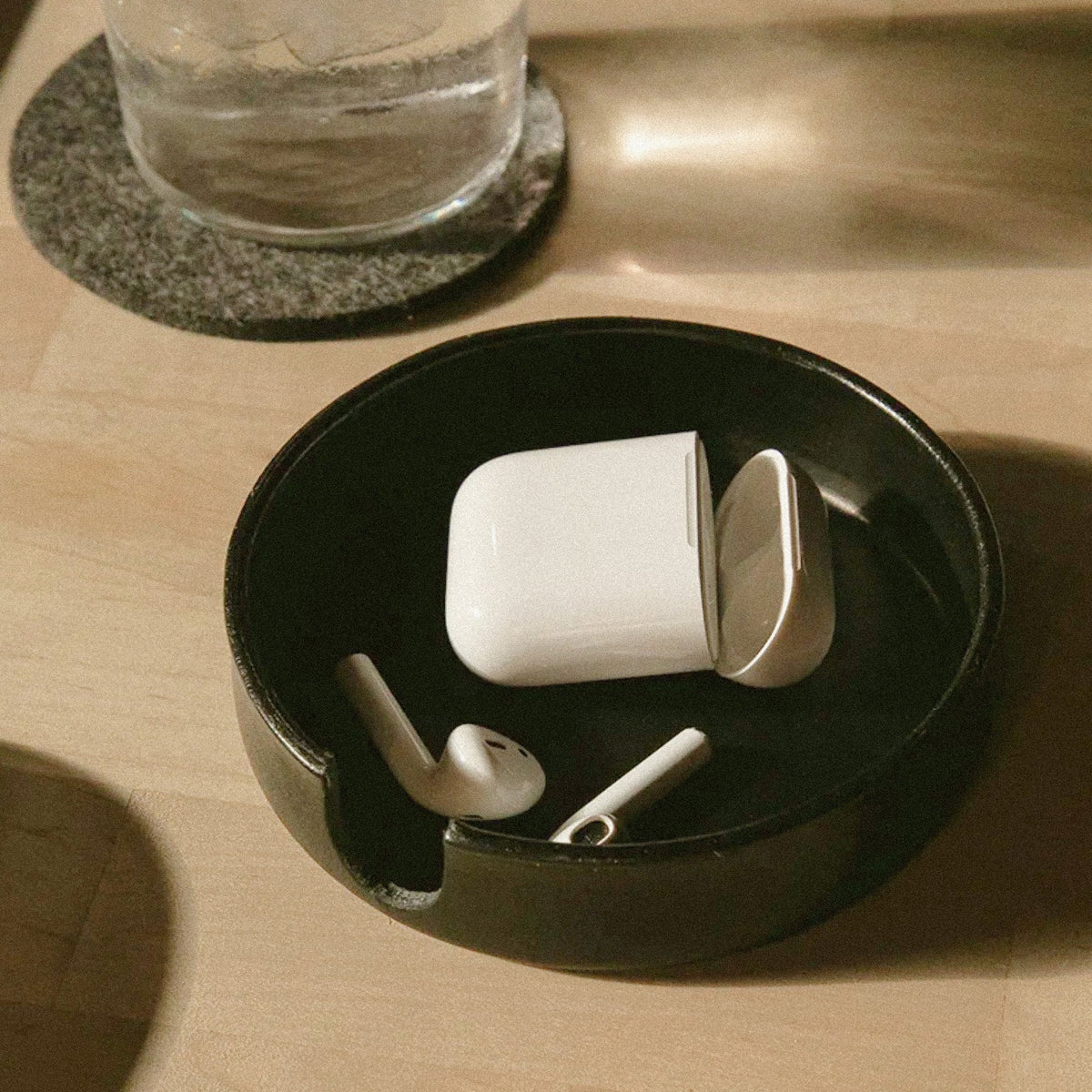 Graf Lantz Black Kobon round leather tray holding earbuds on a wooden desk
