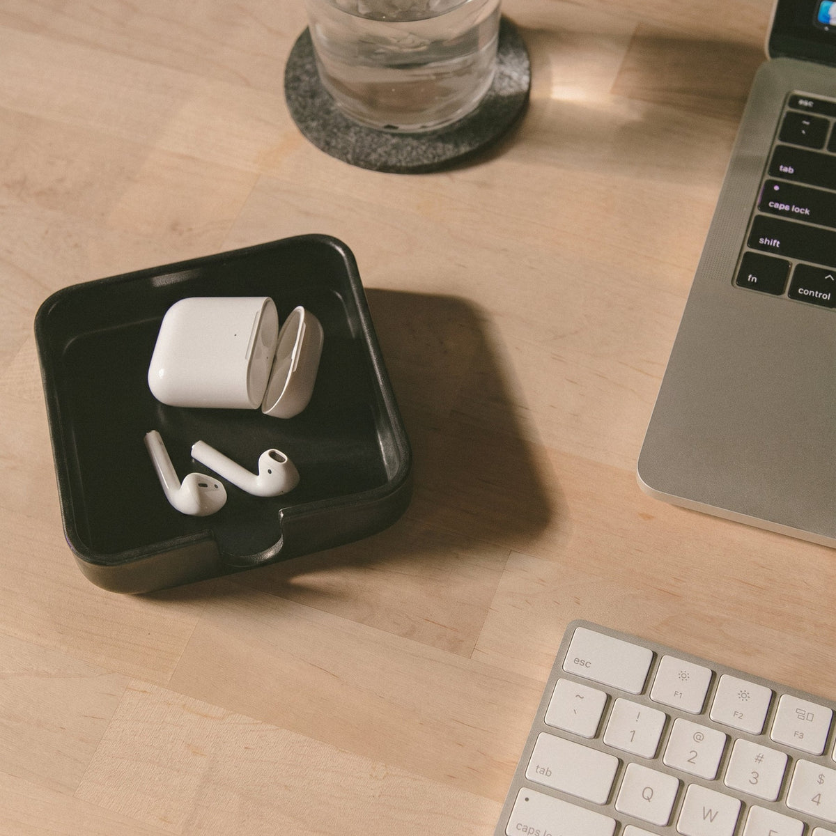 Graf Lantz Black Kobon square leather tray holding earbuds on a desk beside a keyboard