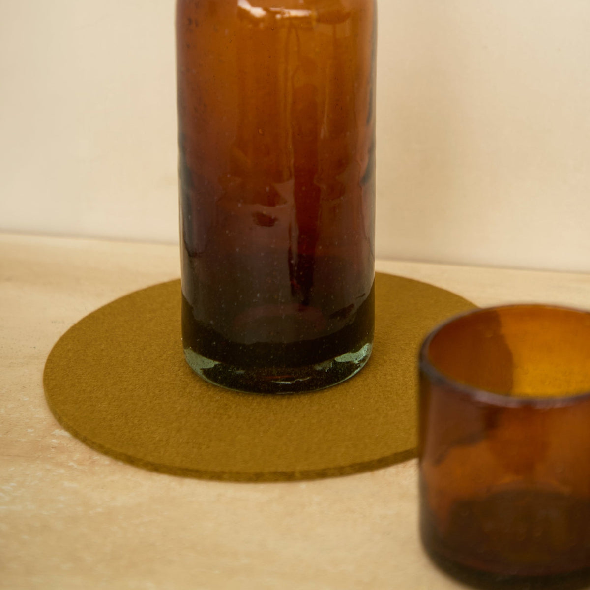 Graf Lantz Brine round felt trivet beneath an amber glass bottle beside a drinking glass
