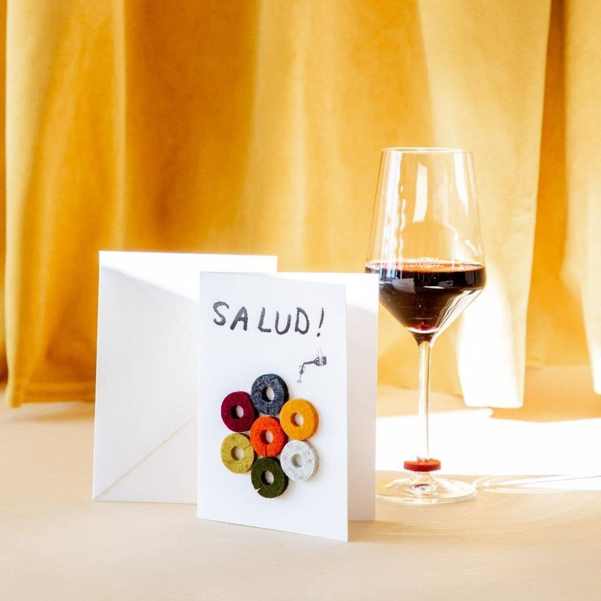 Graf Lantz Salud Wine-Ote’s card beside a glass of red wine and a gold curtain