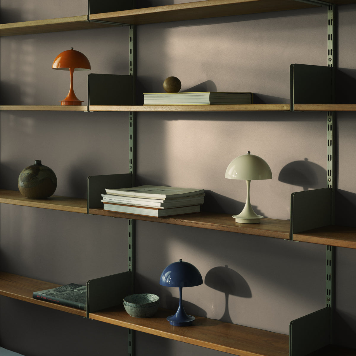 Panthella 160 Portable lamps in several finishes displayed on shelves with books and ceramics.