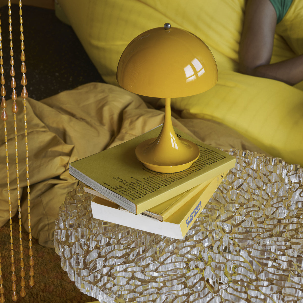 Opaque Yellow Panthella 160 Portable lamp on books beside a yellow sofa.