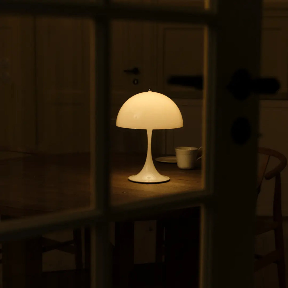 Opal White Panthella 250 Portable Lamp glowing on a windowsill beside a cup.