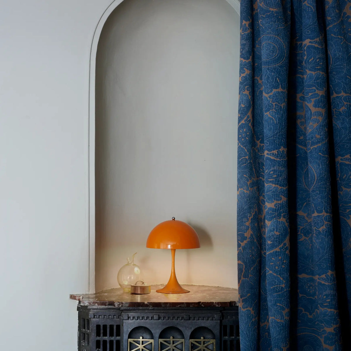 Opaque Orange Panthella 250 Portable Lamp on a decorative chest beside a curtain.