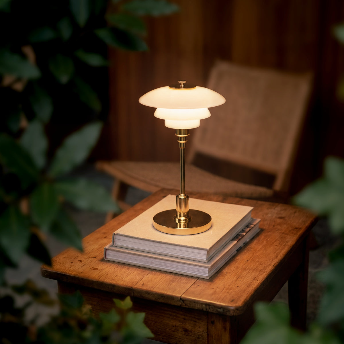Brass PH 1/1 Portable Lamp glowing on books beside an armchair.