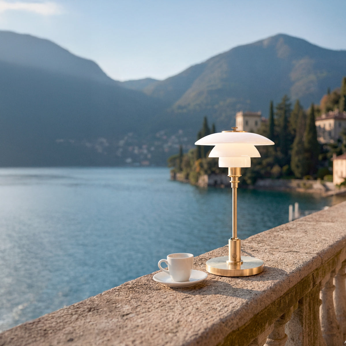 Brass PH 1/1 Portable Lamp beside a cup on a lakeside terrace.