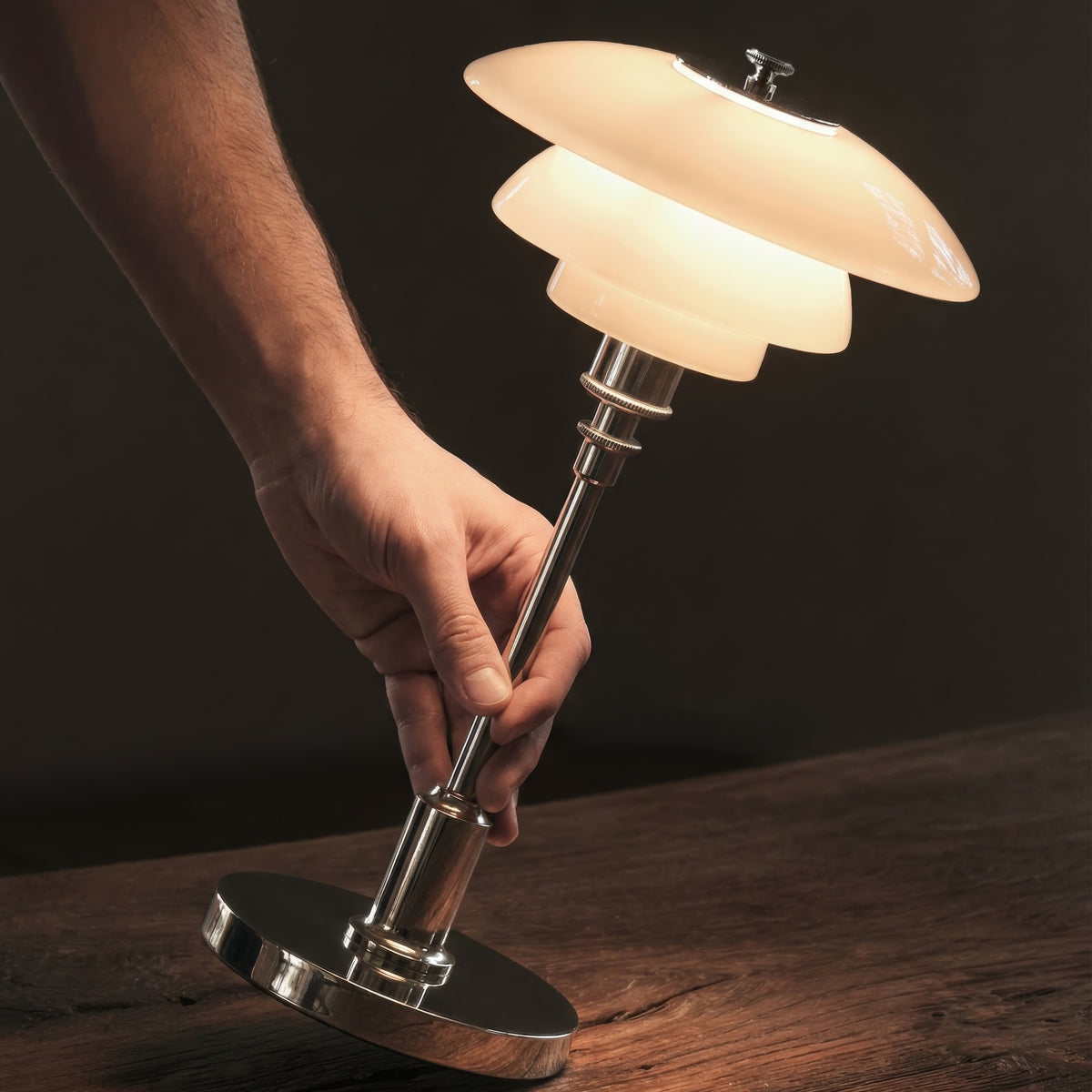 Chrome PH 1/1 Portable Lamp being lifted by its stem, with illuminated opal glass shades.