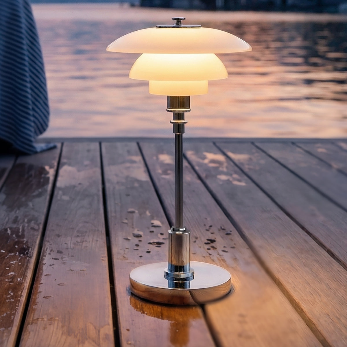 Chrome PH 1/1 Portable Lamp glowing on a wooden deck by the lake.