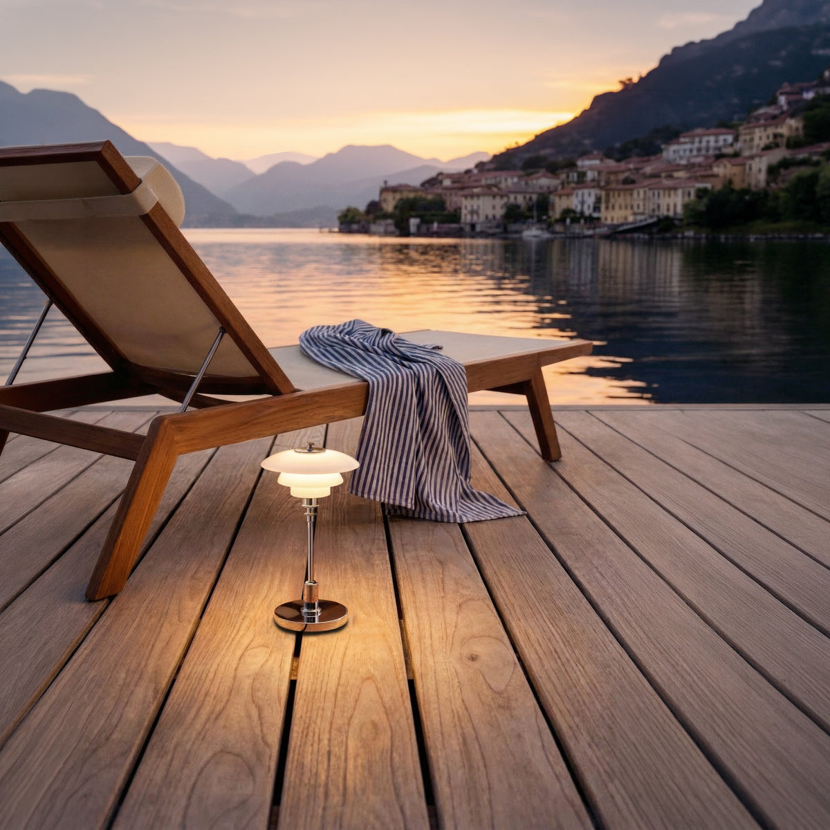 Chrome PH 1/1 Portable Lamp beside a lounge chair overlooking the lake at dusk.