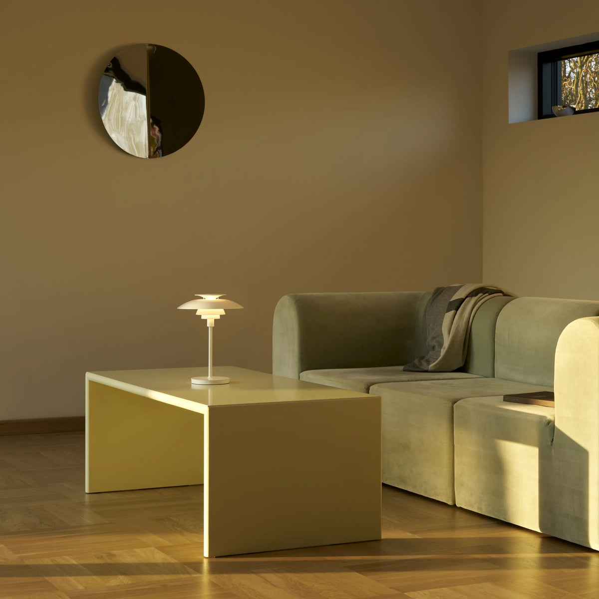 White PH 80 Portable Lamp illuminated beside a sofa in a sunlit living room.