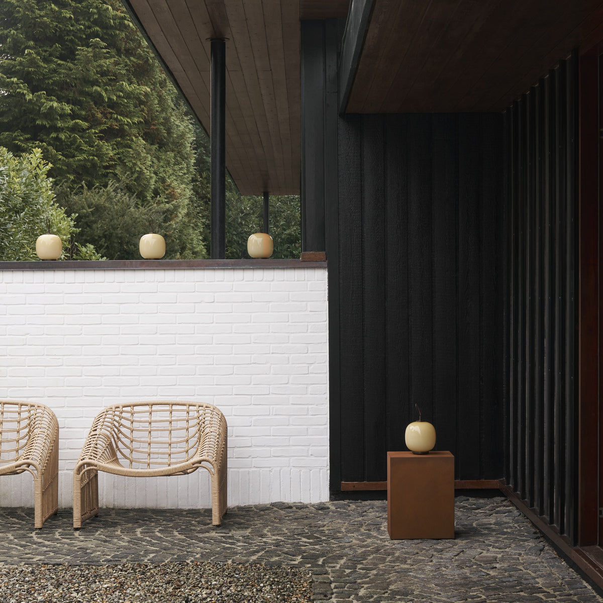 Louis Poulsen VL45 portable lamps arranged on a terrace ledge and pedestal outside a timber-clad home.