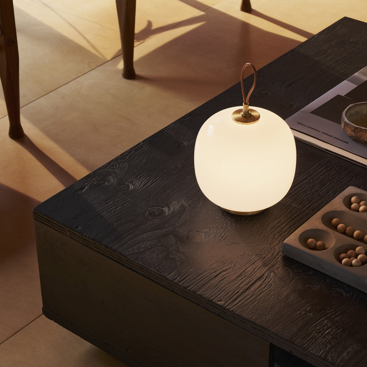 Illuminated Pale Rose VL45 Portable Lamp on a dark wood coffee table in a sunlit living room.