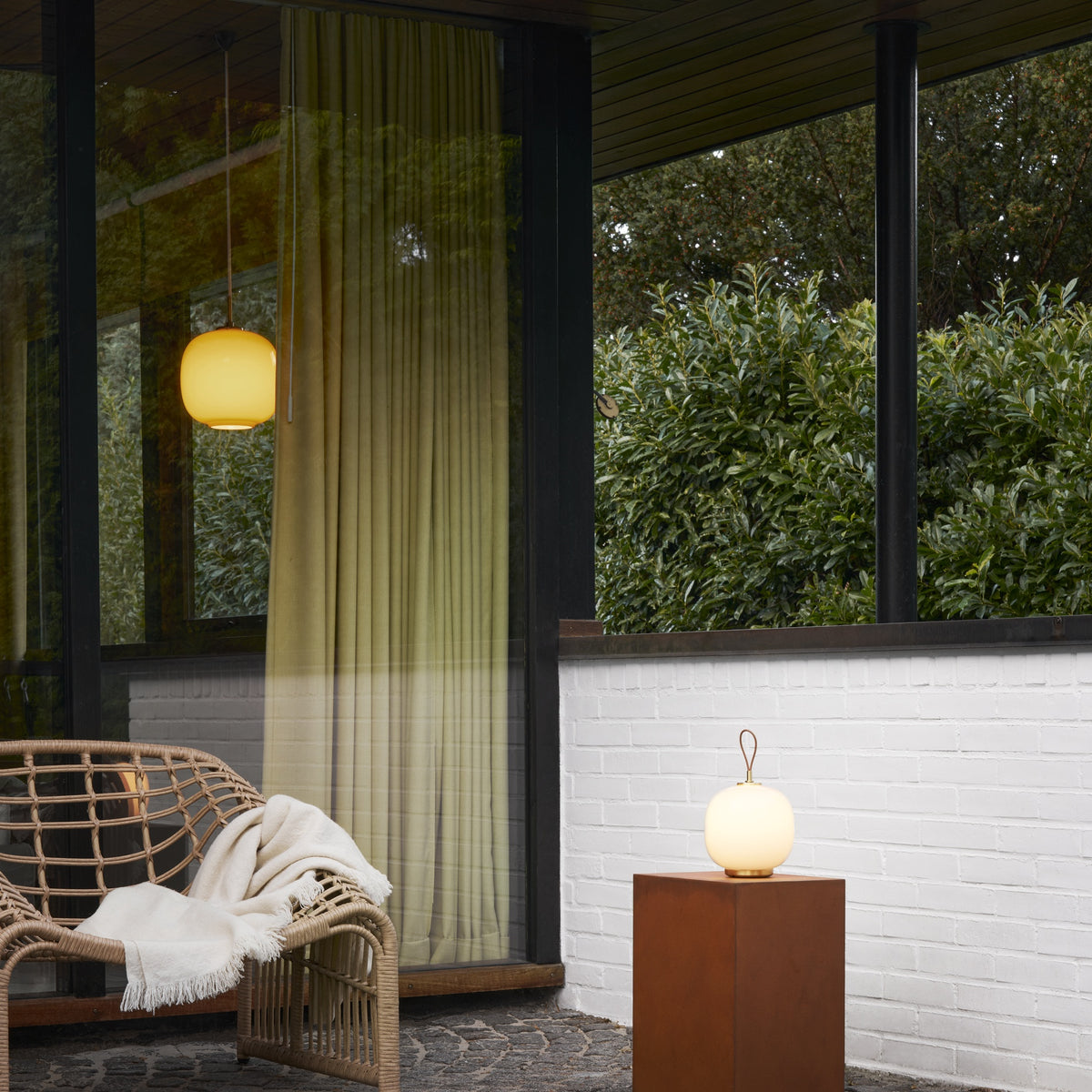 White Opal VL45 Portable Lamp illuminated on a terrace pedestal, with a separate pendant in the background.