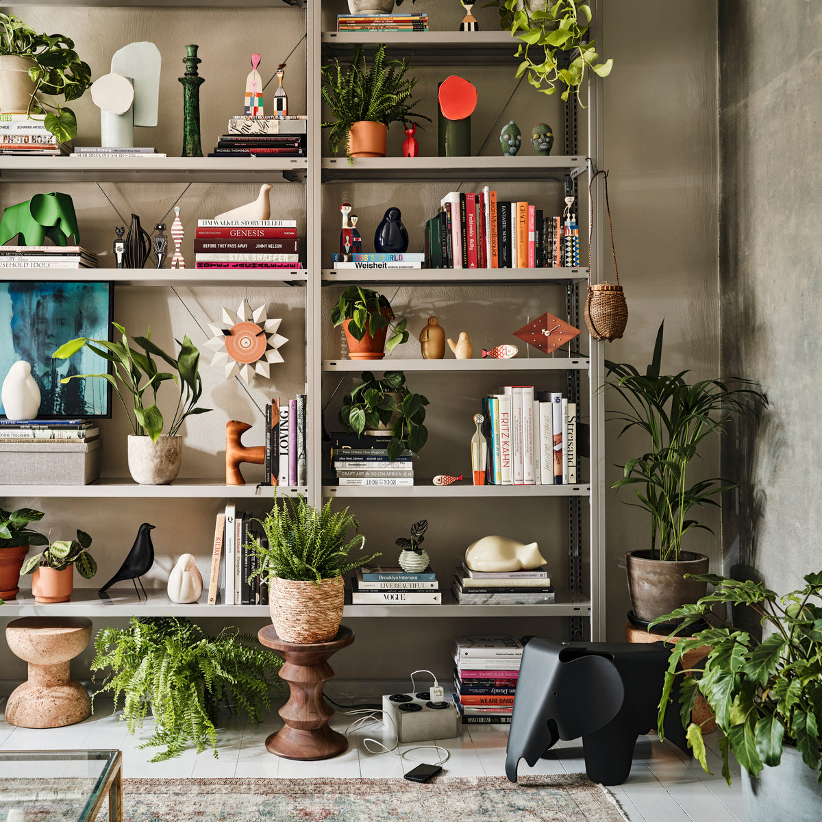 Black Eames Elephant displayed on the floor beside shelves of Vitra accessories